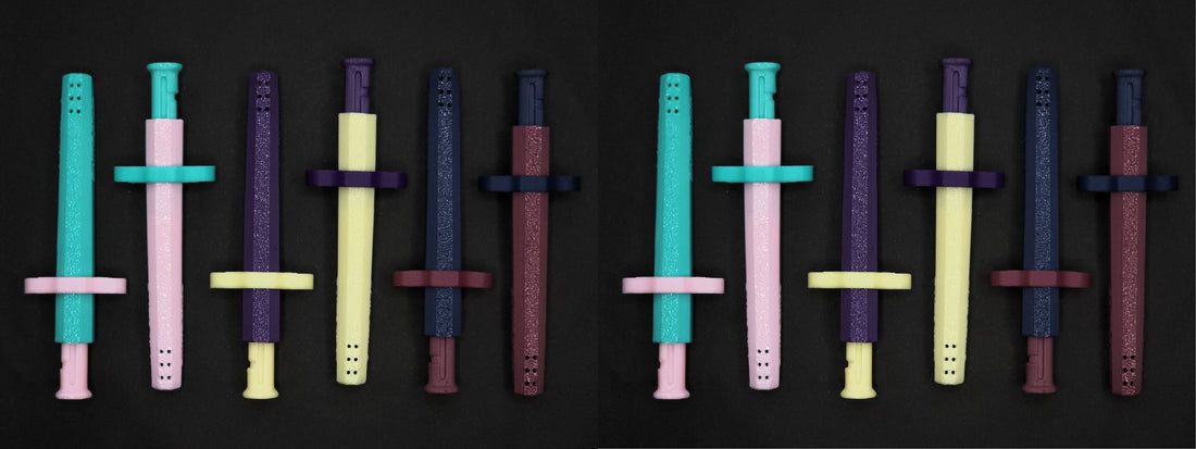 A collection of 12 multi colored Sniff & Slide spring loaded bump straw pendants, From the Color Remix Collection, arranged in a line.
