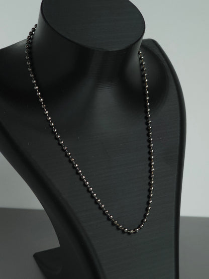 A zoomed in photo of a stock Sniff and Slide bump straw necklace, with black beaded chain necklace displayed on a matte black jewelry bust against a light gray background.