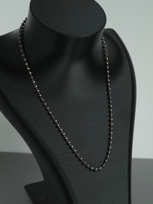 A zoomed in photo of a stock Sniff and Slide bump straw necklace, with black beaded chain necklace displayed on a matte black jewelry bust against a light gray background.