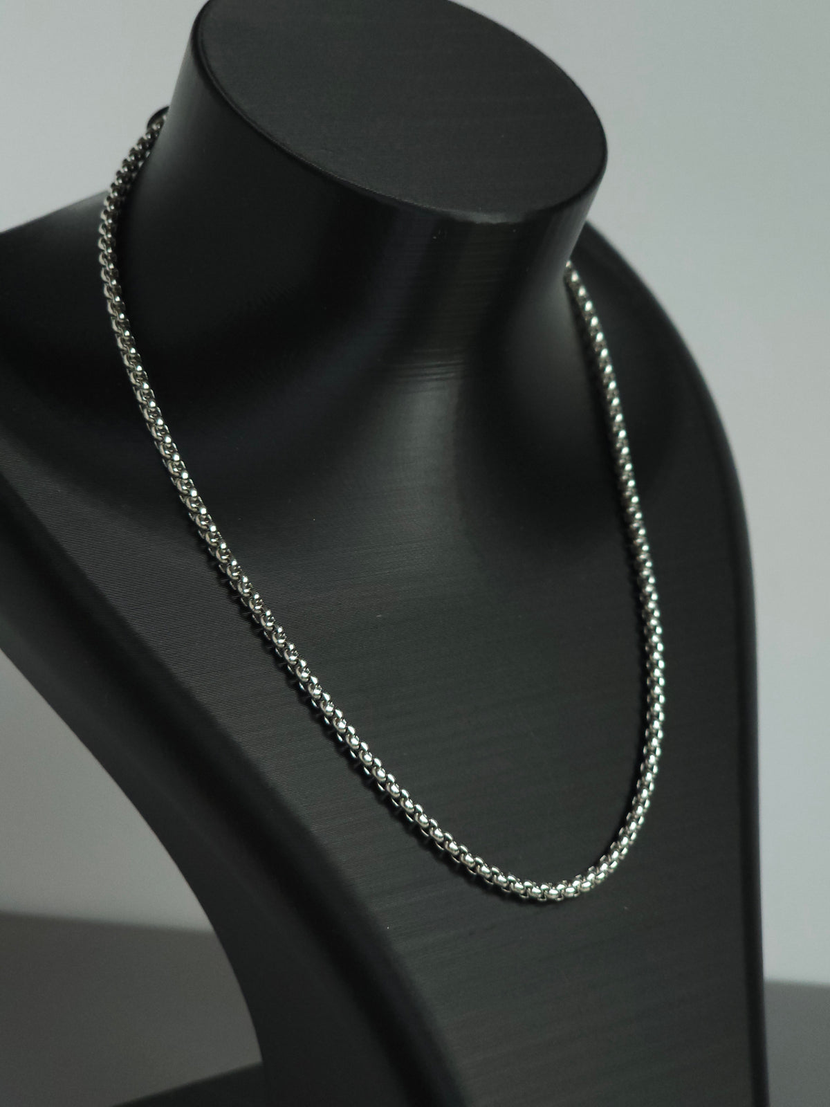 A zoomed in view of a silver-toned chain necklace displayed on a matte black jewelry bust against a light gray background. An upgrade to the stock Sniff and Slide spice straw necklace