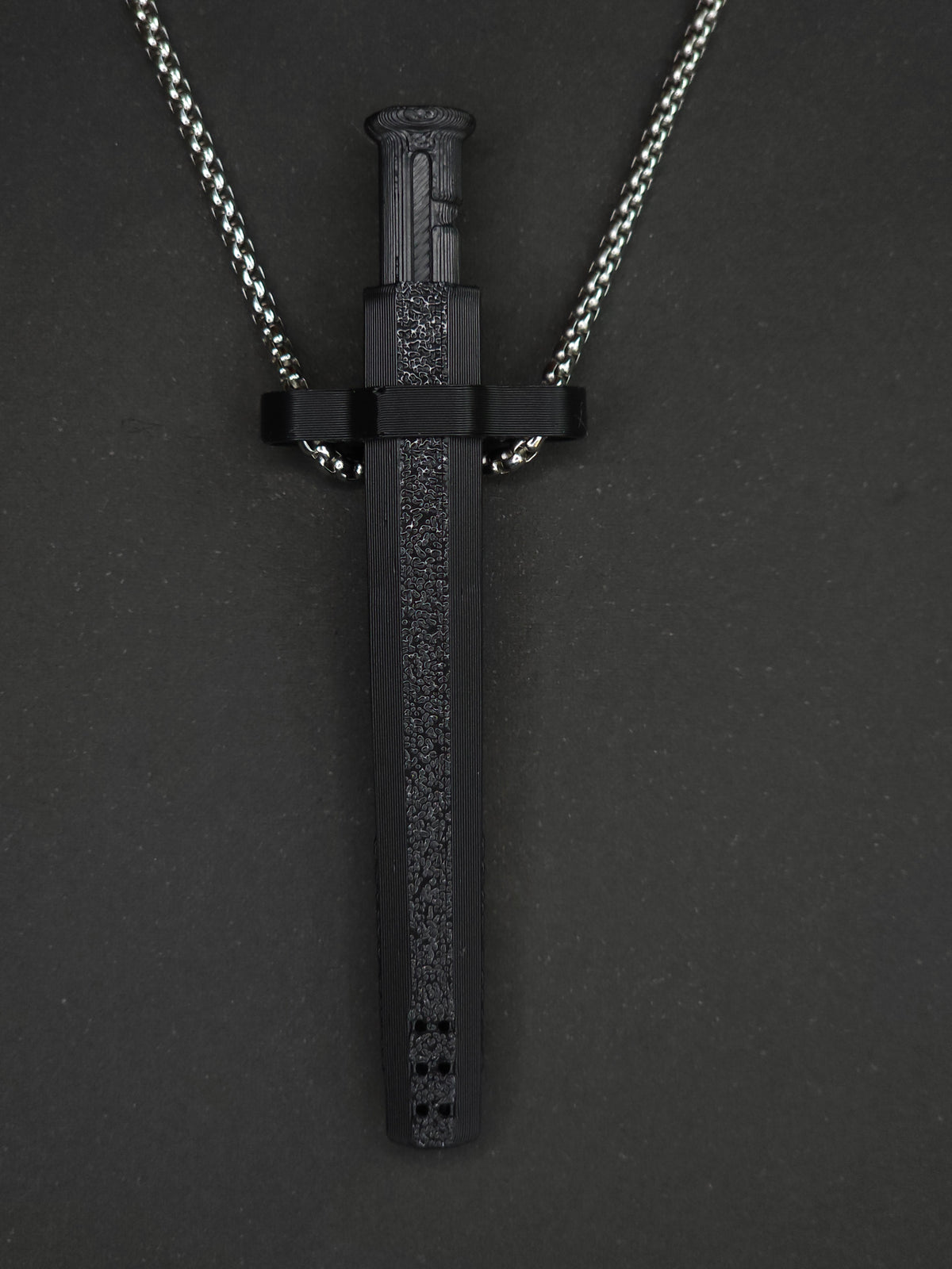 A black spring-loaded bump straw pendant on a silver box chain, displayed against a dark textured background