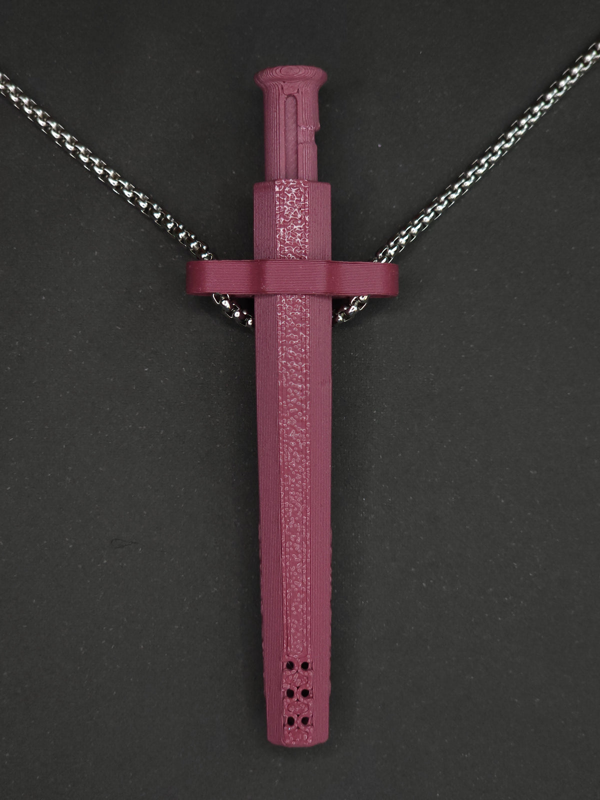 A burgundy spring-loaded bump straw pendant on a silver box chain, displayed against a dark textured background