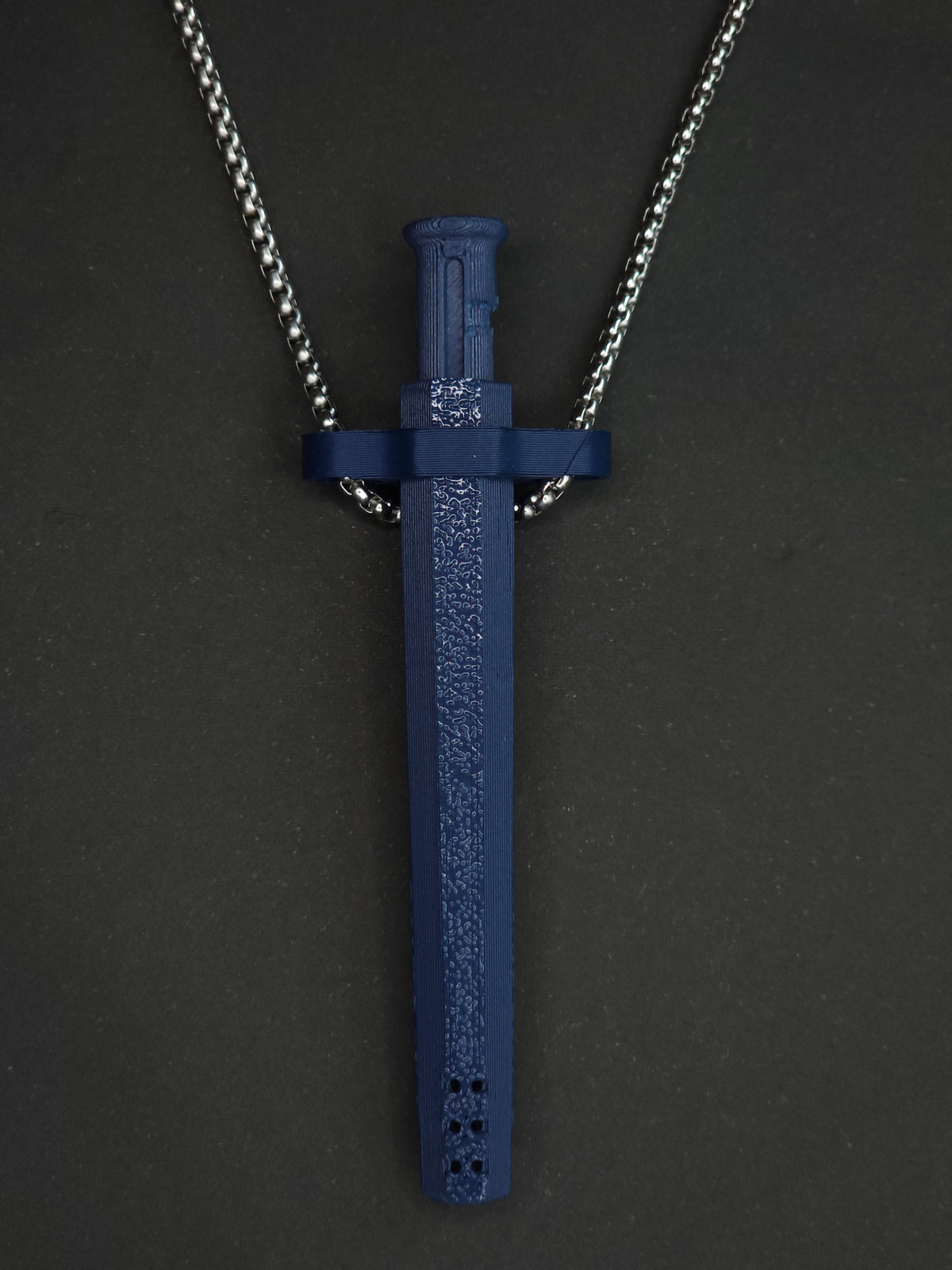 A navy blue spring-loaded bump straw pendant on a silver box chain, displayed against a dark textured background