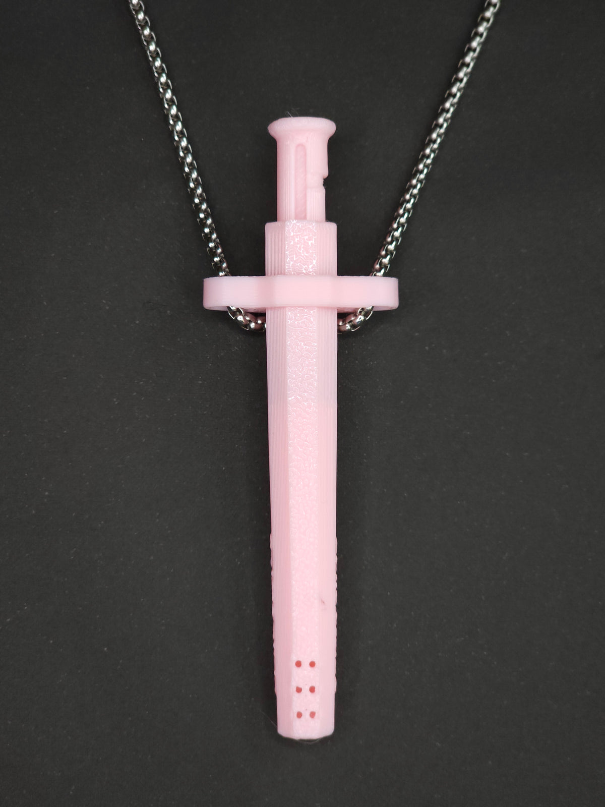 A pink spring-loaded bump straw pendant on a silver box chain, displayed against a dark textured background