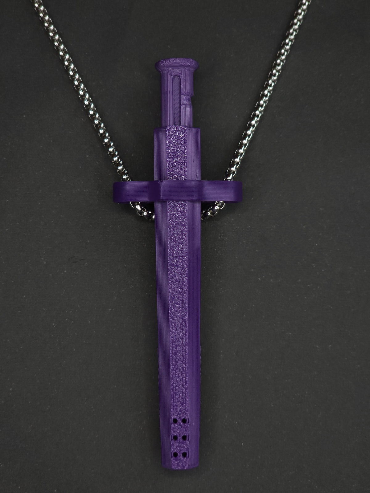 A purple spring-loaded bump straw pendant on a silver box chain, displayed against a dark textured background