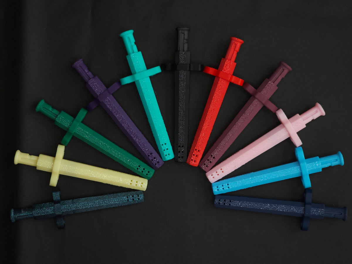 A set of 11 spring loaded bump straw Sniff & Slide Color Remix necklace pendants arranged in a fan shape on a black background, showing multiple colors including yellow, green, teal, purple, black, red, pink, brown, light blue, and dark blue.