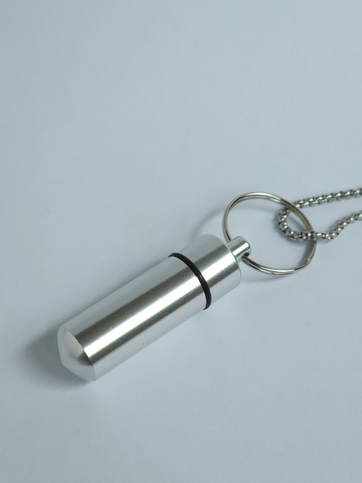A silver metal pendant discreet snuff storage necklace with a threaded cylindrical design, to be paired with the Sniff and Slide, shown closed, attached to a silver ball chain on a light gray background.
