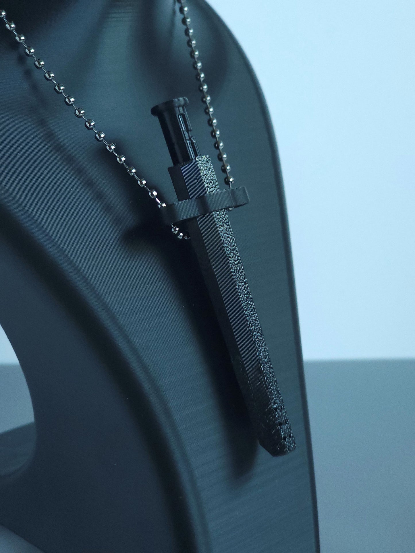 A closeup of  Sniff & Slide spring-loaded bump straw in Onyx Black with silver ball chain, displayed on black mannequin bust, over a blurred white and grey background