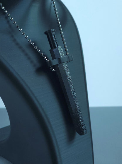 A closeup of  Sniff & Slide spring-loaded bump straw in Onyx Black with silver ball chain, displayed on black mannequin bust, over a blurred white and grey background