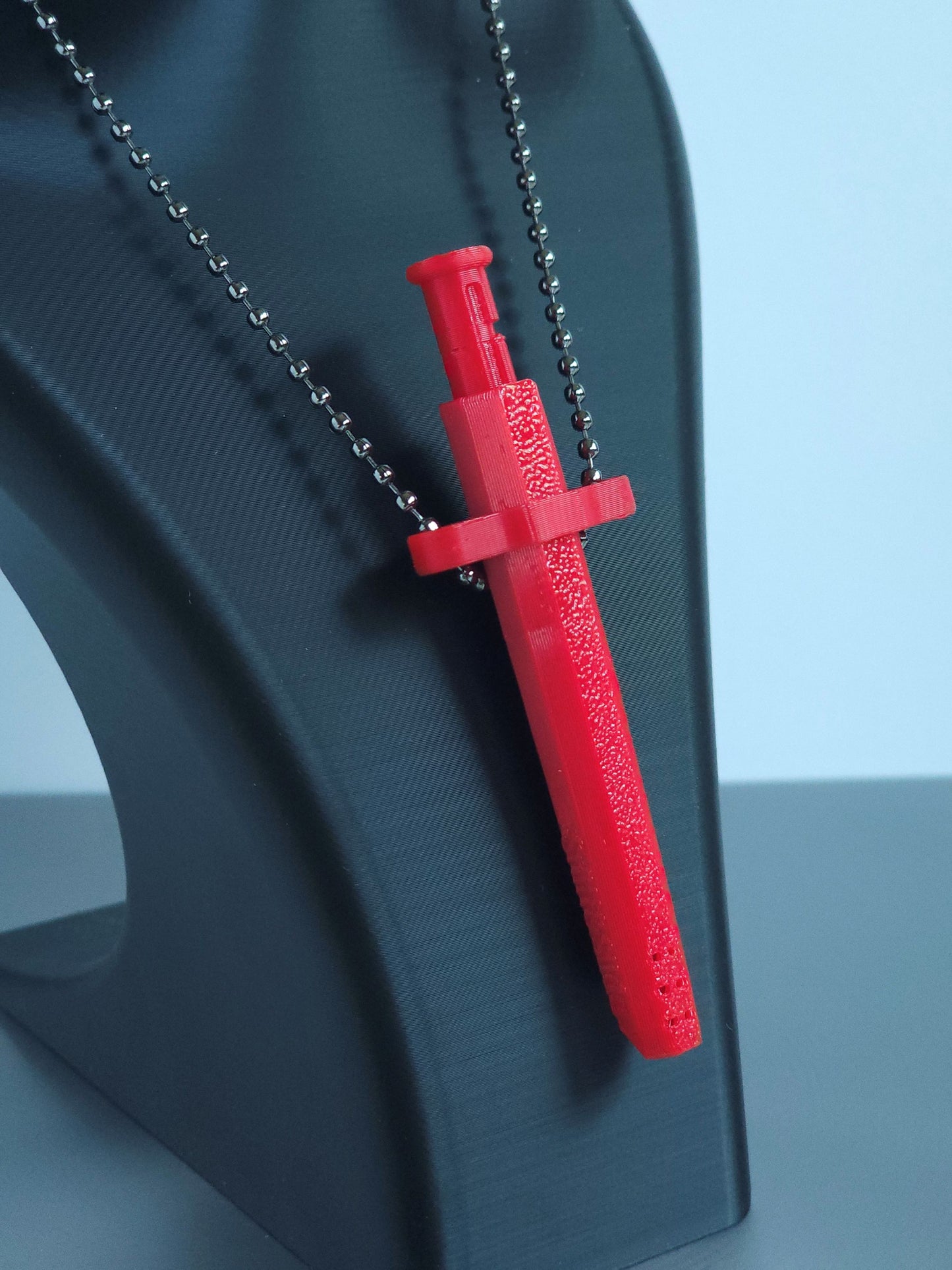 A closeup Sniff & Slide spring-loaded dispenser pendant in a vibrant Red with silver ball chain, displayed on black mannequin bust, over a white and grey background